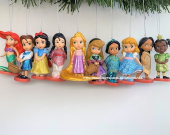 Pode incluir: Conjunto de 10 enfeites de Disney Princess com personagens como Ariel, Bela, Branca de Neve, Mulan, Rapunzel, Aurora, Jasmine, Cinderela, Pocahontas e Tiana. Cada enfeite é feito de plástico e tem um acabamento brilhante.