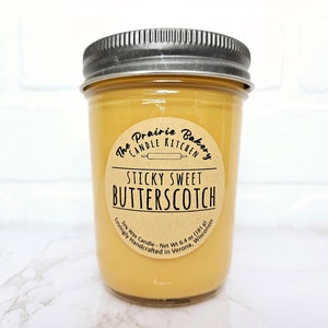 May include: A jar candle with a silver lid filled with a light amber wax. The label reads "Sticky Sweet Butterscotch" from The Prairie Bakery Candle Kitchen. The candle is 6.4 oz (181 g) and made with soy wax.