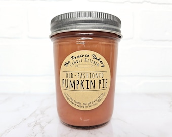 May include: A brown glass jar candle with a brown paper label that reads "The Prairie Bakery Candle Kitchen Old-Fashioned Pumpkin Pie Lovingly Handcrafted in Verona, Wisconsin Soy Wax Candle - Net Wt 6.4 oz (181 g)"