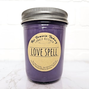 May include: Purple soy wax candle in a glass jar with a brown label that reads "The Prairie Bakery Candle Kitchen" and "Love Spell". The label also includes the text "Soy Wax Candle - Net Wt 6.4 oz (181 g) Lovingly Handcrafted in Verona, Wisconsin."