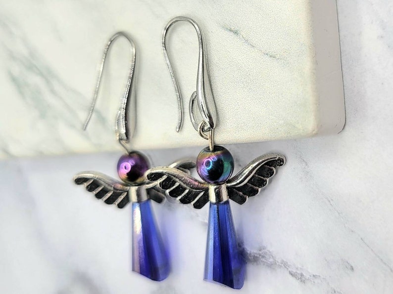 May include: A pair of silver angel dangle earrings with iridescent purple beads and blue crystal drops.
