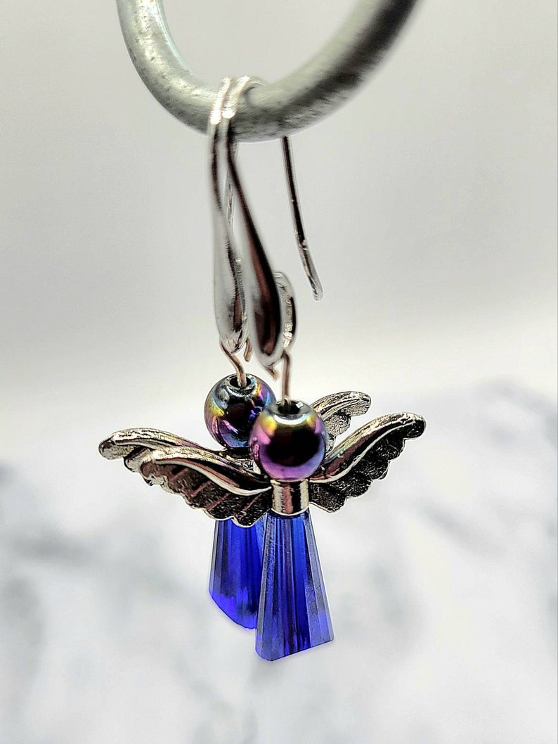May include: A pair of silver angel dangle earrings with iridescent blue glass beads and blue crystal drops.