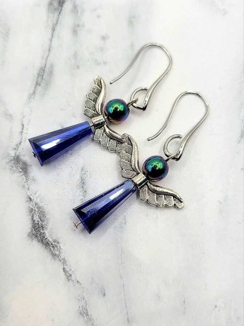 May include: A pair of silver angel wing earrings with iridescent blue beads and dark blue crystal drops.