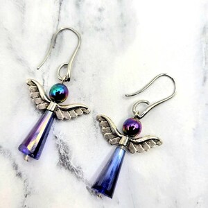 May include: A pair of silver angel wing earrings with iridescent blue glass beads. The beads have a rainbow sheen.