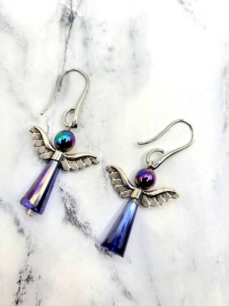 May include: A pair of silver angel wing earrings with iridescent blue glass beads. The beads have a rainbow sheen.