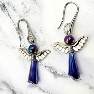 May include: A pair of silver angel dangle earrings with iridescent purple beads and dark blue crystal drops.