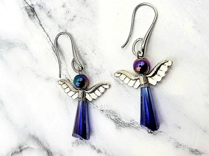 May include: A pair of silver angel dangle earrings with iridescent purple beads and dark blue crystal drops.