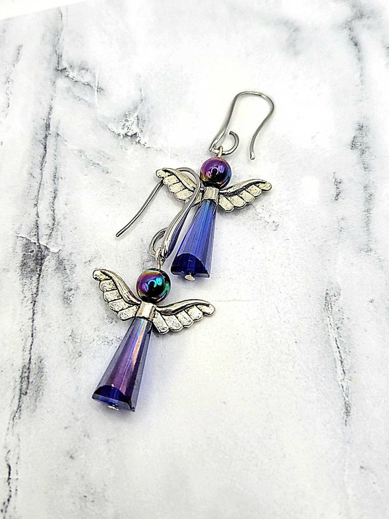 May include: A pair of silver angel earrings with iridescent purple and blue crystal drops.