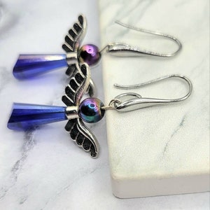 May include: A pair of silver angel wing earrings with iridescent blue teardrop crystals and black beads.