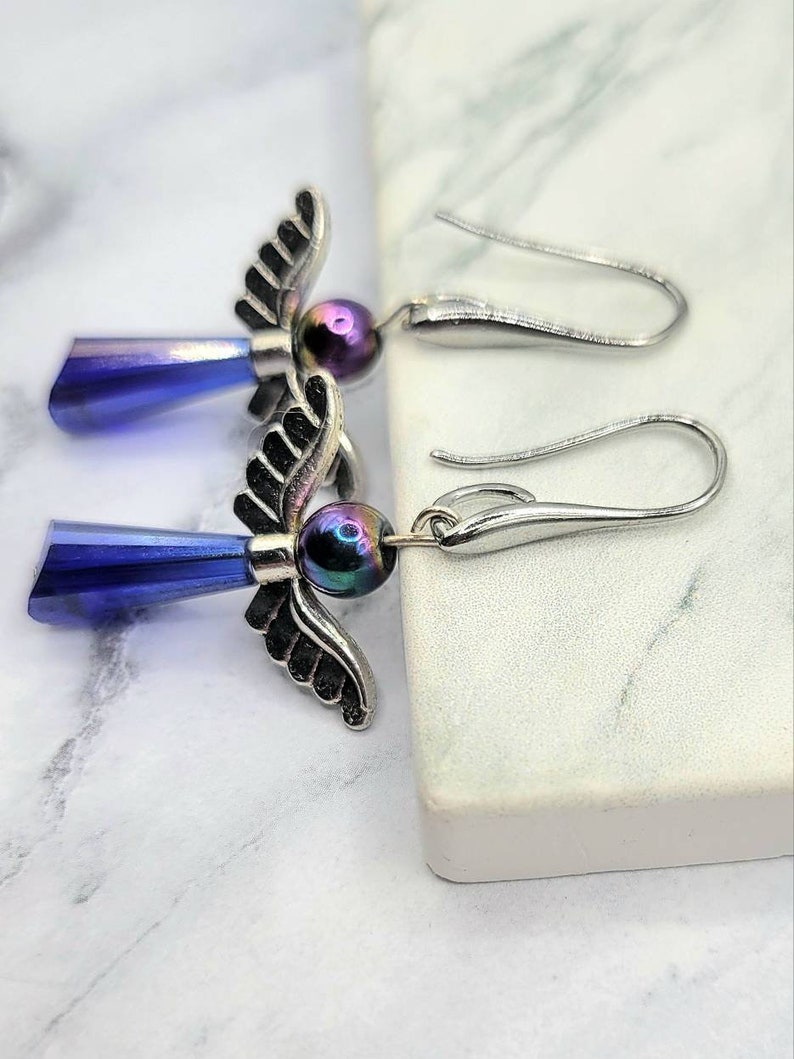 May include: A pair of silver angel wing earrings with iridescent blue teardrop crystals and black beads.