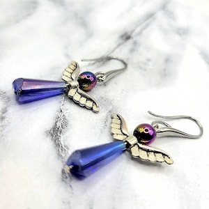 May include: A pair of silver angel wing earrings with iridescent blue teardrop crystals and iridescent purple beads.