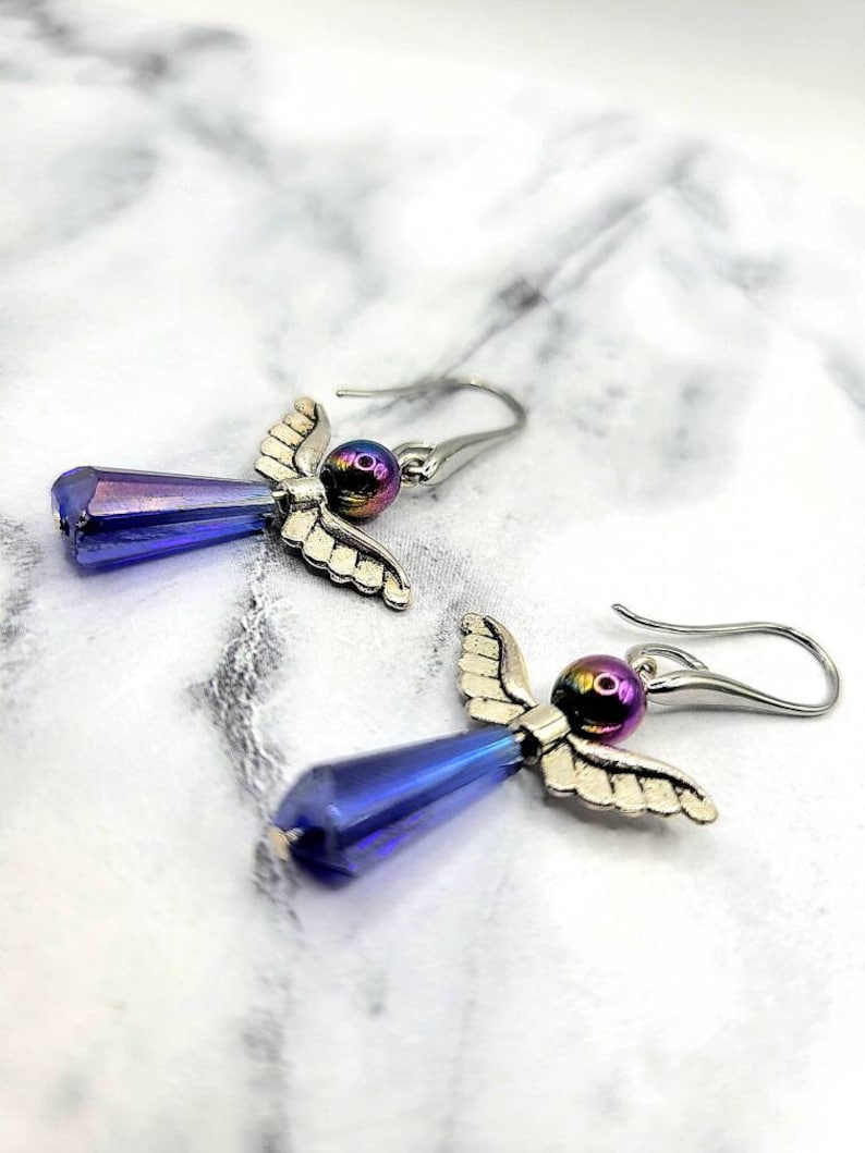May include: A pair of silver angel wing earrings with iridescent blue teardrop crystals and iridescent purple beads.