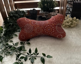 May include: Bone-shaped cushion with a red and white mandala pattern. The cushion is made of soft fabric and is designed for comfort. The cushion is a decorative item that can be used in various settings.