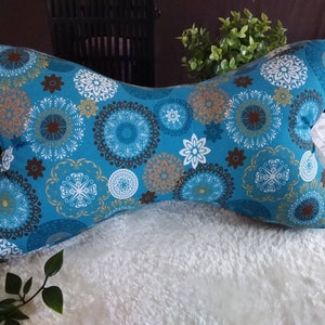 Op de afbeelding: Een blauw en wit gepatroneerd kussen met een strikvorm. Het kussen heeft verschillende ronde ontwerpen in tinten bruin, wit en blauw.