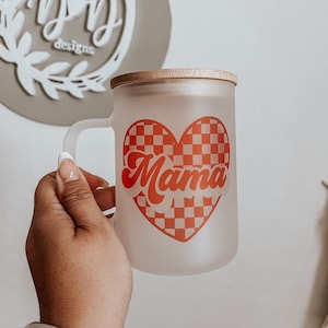 May include: A frosted glass mug with a bamboo lid. The mug has a red checkered heart with the word "Mama" in a retro font.