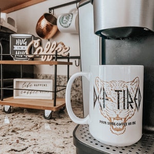 Pu&ograve; includere: Tazza da caff&egrave; bianca con stampa di ghepardo dorata e il testo "De-Tired" e "Versami un po' di caff&egrave;".