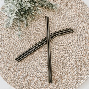 May include: Four black metal reusable drinking straws on a woven straw placemat.