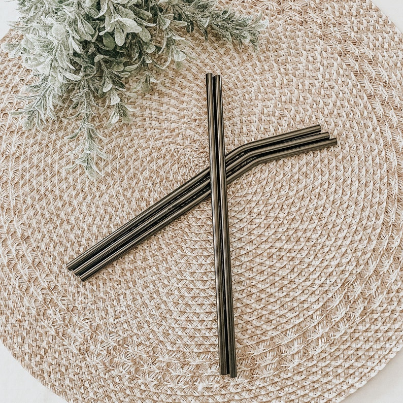 May include: Four black metal reusable drinking straws on a woven straw placemat.