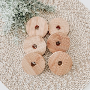 May include: Six wooden round coasters with a hole in the center. The coasters are stacked on top of each other and are arranged in a circle on a woven surface.
