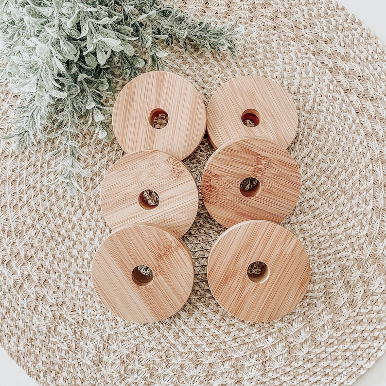 May include: Six wooden round coasters with a hole in the center. The coasters are stacked on top of each other and are arranged in a circle on a woven surface.