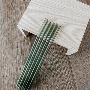 May include: A set of six green glass drinking straws. The straws are bundled together and have a slightly iridescent sheen.