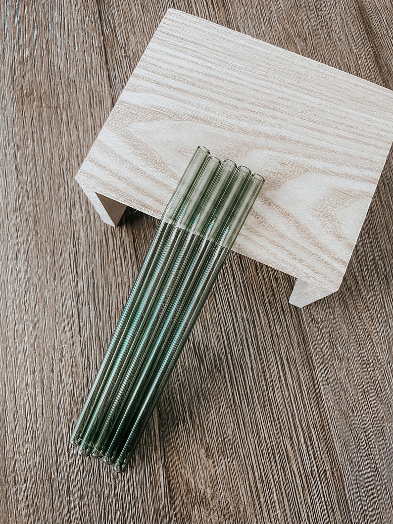 May include: A set of six green glass drinking straws. The straws are bundled together and have a slightly iridescent sheen.