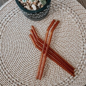 May include: Four brown glass reusable drinking straws on a woven straw placemat.