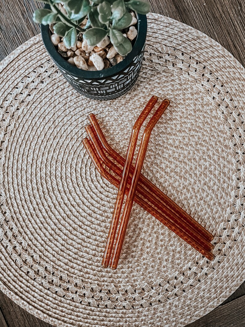 May include: Four brown glass reusable drinking straws on a woven straw placemat.