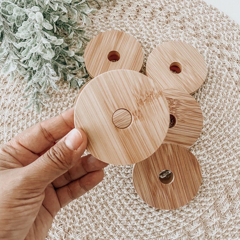 May include: Five round wooden coasters with a hole in the center. The coasters are stacked on top of each other and are made of light brown wood.