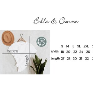 May include: A white t-shirt hanging on a wooden hanger, with a tan hat to the left. The shirt's width ranges from 18 to 28 inches, and the length from 27 to 33 inches. The text "Bella & Canvas" is at the top.