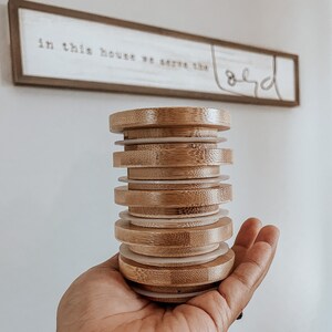 May include: A stack of eight round, wooden, bamboo lids with white rings in between each lid. The lids are stacked in a person's hand.