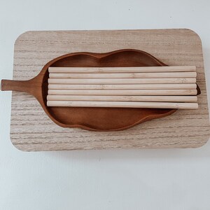 May include: A wooden tray in the shape of a leaf with a stack of natural bamboo drinking straws inside.