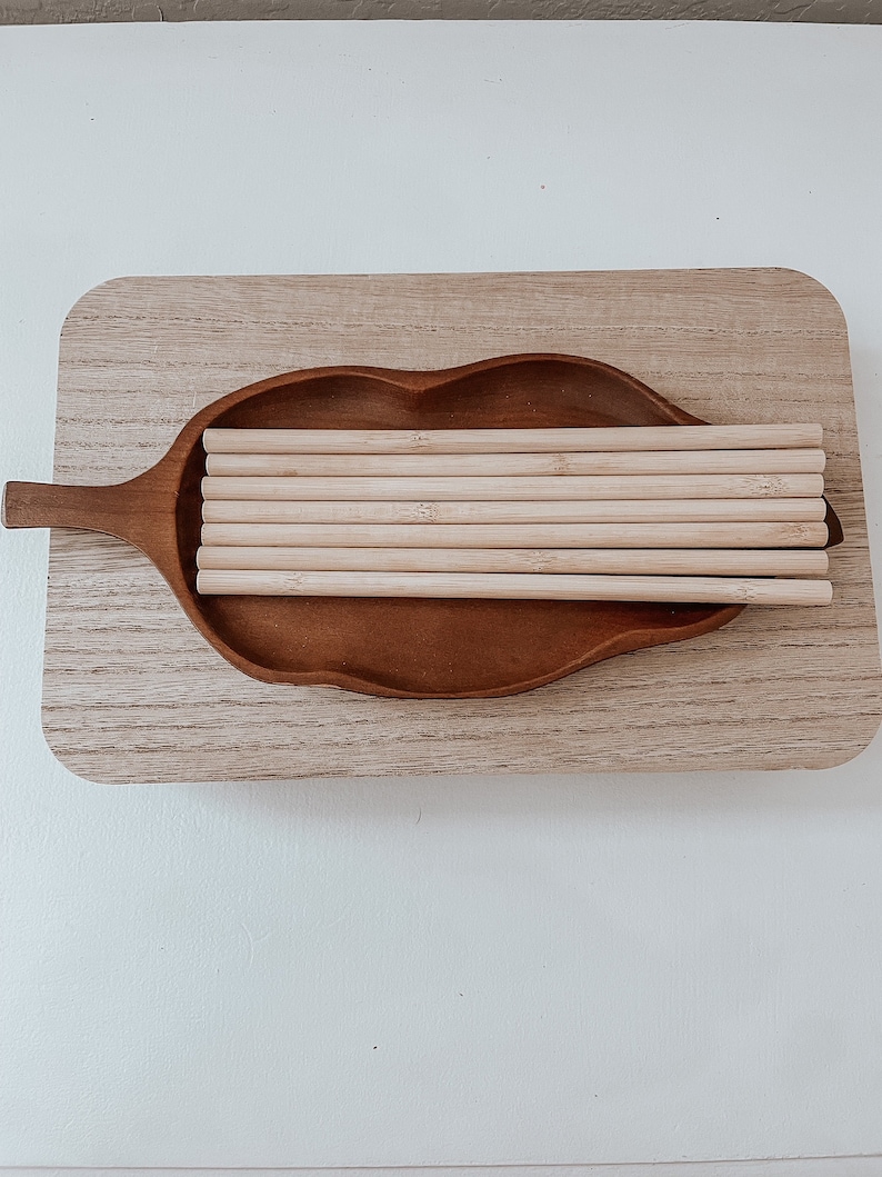 May include: A wooden tray in the shape of a leaf with a stack of natural bamboo drinking straws inside.