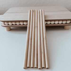 May include: A set of eight natural bamboo drinking straws. The straws are arranged in a row on a white surface.