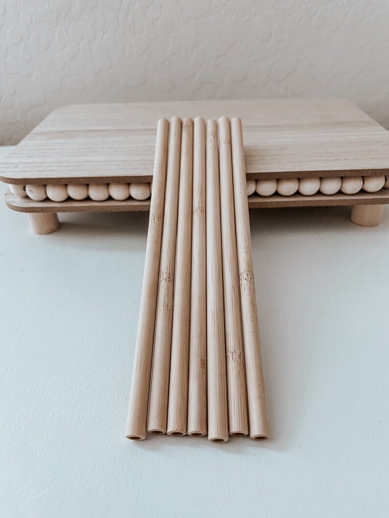 May include: A set of eight natural bamboo drinking straws. The straws are arranged in a row on a white surface.
