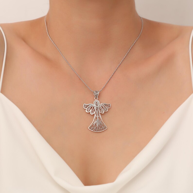 Pu&ograve; includere: Una collana con ciondolo a forma di angelo in filigrana d'argento. L'angelo &egrave; decorato con disegni intricati e ha un aspetto delicato e femminile.