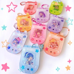 May include: A selection of vibrant, retro-themed keychain charms. Each charm showcases a unique anime-style character illustration encased in clear plastic. The charms come in a variety of colours, such as pink, yellow, green, and blue, and are decorated with star-shaped embellishments.