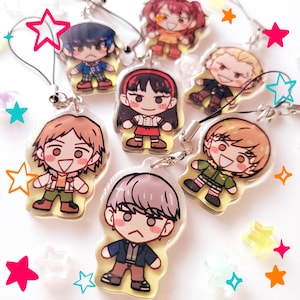May include: A selection of cartoon character acrylic charms. Each charm depicts a different character with distinct outfits and expressions. The charms are attached to black lanyards and surrounded by colourful star-shaped decorations.