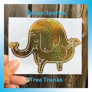 Peut inclure: Autocollant blanc avec un &eacute;l&eacute;phant scintillant jaune. Le texte "Yellow Sparkle" et "Tree Trunks" est &eacute;galement visible. L'&eacute;l&eacute;phant a un design fantaisiste avec une trompe, des oreilles et un n&oelig;ud sur sa queue.