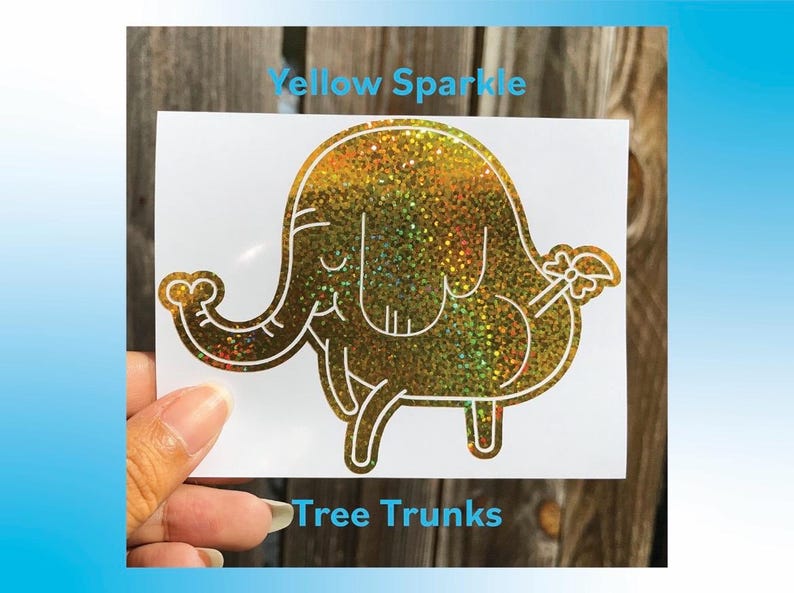 Peut inclure: Autocollant blanc avec un &eacute;l&eacute;phant scintillant jaune. Le texte "Yellow Sparkle" et "Tree Trunks" est &eacute;galement visible. L'&eacute;l&eacute;phant a un design fantaisiste avec une trompe, des oreilles et un n&oelig;ud sur sa queue.