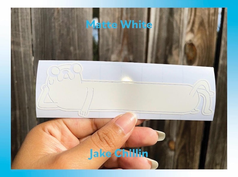 Peut inclure: Autocollant en vinyle blanc mat repr&eacute;sentant un personnage de dessin anim&eacute; dans une pose d&eacute;tendue. L'autocollant porte le texte "Jake Chillin" et "Matte White". L'autocollant est tenu par une main.