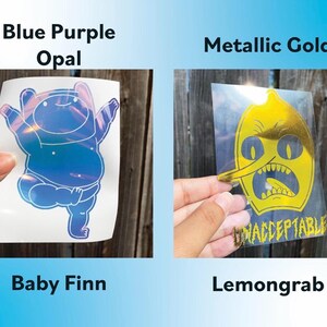 Peut inclure: Deux autocollants en vinyle sont pr&eacute;sent&eacute;s. L'un est un Baby Finn opale bleu-violet, et l'autre est un Lemongrab dor&eacute; m&eacute;tallis&eacute;. Le mot "UNACCEPTABLE" est imprim&eacute; sur l'autocollant Lemongrab.
