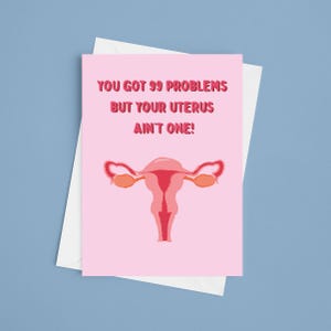 May include: A pink greeting card with the text "YOU GOT 99 PROBLEMS BUT YOUR UTERUS AIN'T ONE!" and a stylized illustration of a uterus. The card is inside a white envelope, set against a blue background.