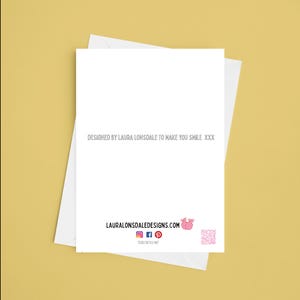 May include: A white greeting card with a matching envelope, set against a yellow background. The card features the text "DESIGNED BY LAURA LONSDALE TO MAKE YOU SMILE XXX" in gray. The bottom of the card displays the website address and social media icons.