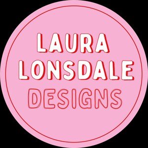May include: A round pink sticker with the text "LAURA LONSDALE DESIGNS" in white, outlined in red. The sticker has a simple, bold design, perfect for branding or product labeling.