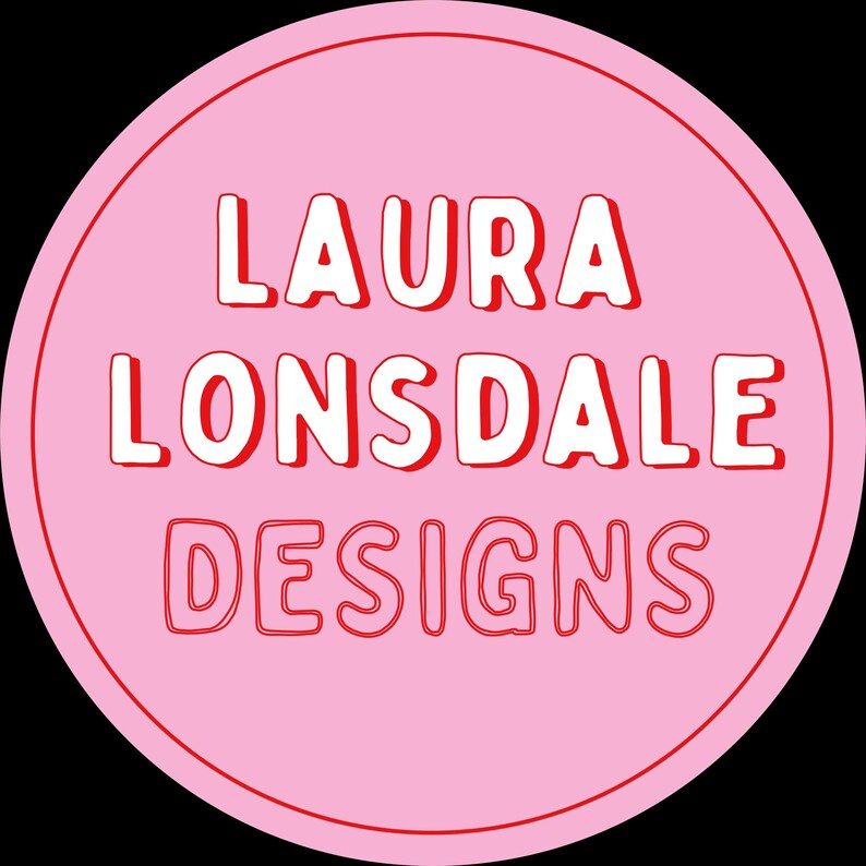 May include: A round pink sticker with the text "LAURA LONSDALE DESIGNS" in white, outlined in red. The sticker has a simple, bold design, perfect for branding or product labeling.