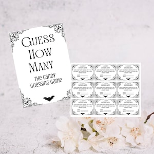 May include: A black and white "Guess How Many" candy guessing game set. The set includes a decorative sign with the game title and a bat silhouette, along with several matching guess cards.