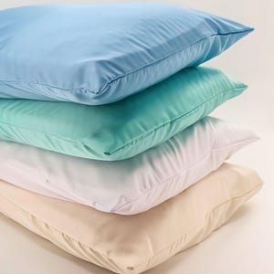 May include: A stack of four pillowcases in different colors: light blue, mint green, white, and beige. The pillowcases are made of a soft, smooth fabric.