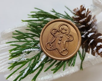 May include: A gold wax seal with a gingerbread man design on a white background with green pine branches and a brown pine cone.