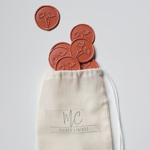 May include: A small white drawstring bag with the text "MC SILVER LININGS" printed on the front. The bag is filled with terracotta-colored wax seals with a floral design.